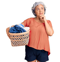 Senior woman with gray hair holding laundry basket serious face thinking about question with hand...