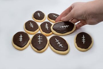 Obraz na płótnie Canvas Football shape cookies. Hand taking cookie. Home made cookies concept. Super Bowl party cookies.