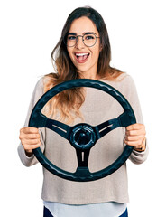 Beautiful hispanic woman holding steering wheel celebrating crazy and amazed for success with open eyes screaming excited.