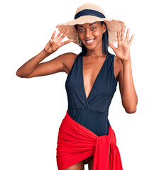 Young african american woman wearing swimsuit and summer hat showing and pointing up with fingers number nine while smiling confident and happy.