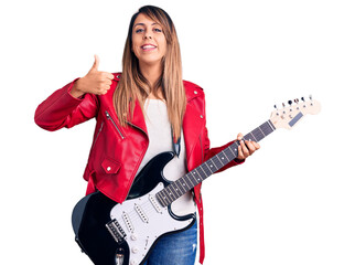 Fototapeta premium Young beautiful woman playing electric guitar smiling happy and positive, thumb up doing excellent and approval sign
