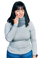 Young hispanic plus size woman wearing winter scarf touching mouth with hand with painful expression because of toothache or dental illness on teeth. dentist