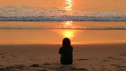 A girl sitting on a sandy beach watching the sunset in Newport Beach city in California