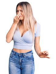 Young beautiful blonde woman wearing casual clothes smelling something stinky and disgusting, intolerable smell, holding breath with fingers on nose. bad smell