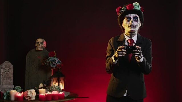 Woman with lady of death body art playing video games in studio, using controller to play on gaming console. Wearing spooky halloween costume of mexican day of the dead tradition.