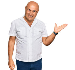 Mature middle east man with mustache wearing casual white shirt smiling cheerful presenting and pointing with palm of hand looking at the camera.