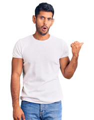 Young latin man wearing casual clothes surprised pointing with hand finger to the side, open mouth amazed expression.