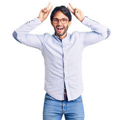Handsome hispanic man wearing business shirt and glasses posing funny and crazy with fingers on head as bunny ears, smiling cheerful