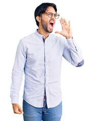 Handsome hispanic man wearing business shirt and glasses shouting and screaming loud to side with hand on mouth. communication concept.