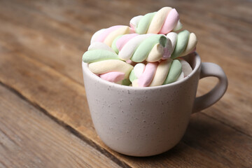 Ceramic cup with colorful marshmallows on wooden table, closeup