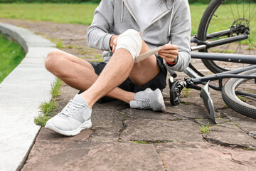 Obraz premium Man applying bandage onto his knee near bicycle outdoors, closeup