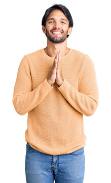 Handsome hispanic man wearing casual sweater praying with hands together asking for forgiveness smiling confident.