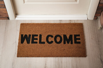 Door mat with word Welcome on wooden floor in hall, above view - obrazy, fototapety, plakaty