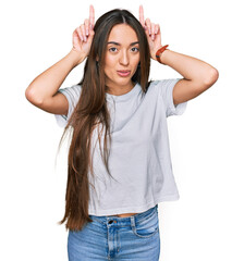 Fototapeta premium Young hispanic girl wearing casual white t shirt doing funny gesture with finger over head as bull horns