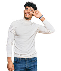 Fototapeta premium Young arab man wearing casual winter sweater doing peace symbol with fingers over face, smiling cheerful showing victory