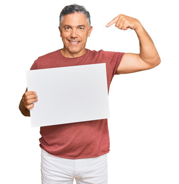 Handsome middle age man holding blank empty banner pointing finger to one self smiling happy and proud
