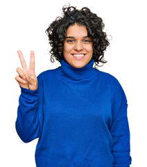Young hispanic woman with curly hair wearing turtleneck sweater showing and pointing up with fingers number two while smiling confident and happy.