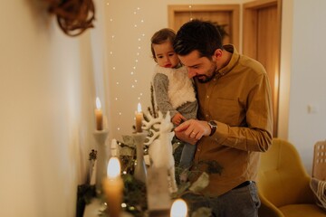Father holding his daughter and pointing at a Christmas ornament of a deer with lit candles.