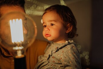 Father holding his daughter looking at a bright light bulb.