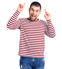Naklejka premium Young handsome man wearing striped sweater smiling amazed and surprised and pointing up with fingers and raised arms.
