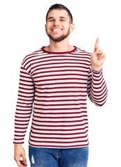Fototapeta premium Young handsome man wearing striped sweater showing and pointing up with finger number one while smiling confident and happy.