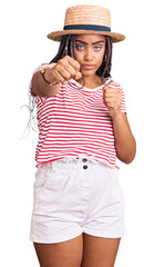 Young african american woman with braids wearing summer hat punching fist to fight, aggressive and angry attack, threat and violence