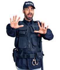 Young hispanic man wearing police uniform afraid and terrified with fear expression stop gesture with hands, shouting in shock. panic concept.