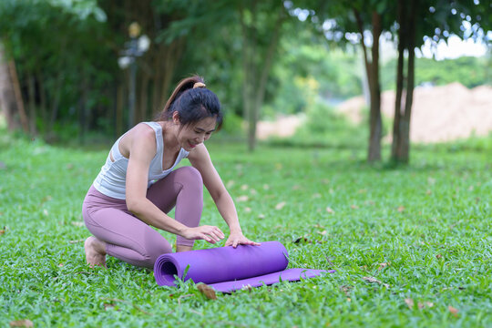 Closeup of attractive young woman folding blue yoga or exercise mat after exercise at park healthy living to fit horizontal image concept.
