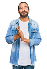 Attractive man with long hair and beard wearing casual denim jacket clapping and applauding happy...