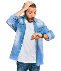 Attractive man with long hair and beard wearing casual denim jacket looking at the watch time...