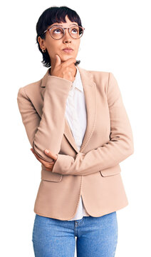 Young brunette woman with short hair wearing business jacket and glasses with hand on chin thinking about question, pensive expression. smiling with thoughtful face. doubt concept.