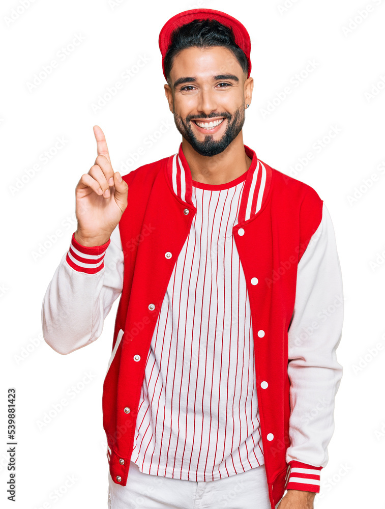 Sticker Young man with beard wearing baseball uniform showing and pointing up with finger number one while smiling confident and happy.