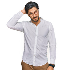 Young hispanic man wearing business shirt and glasses confuse and wonder about question. uncertain with doubt, thinking with hand on head. pensive concept.