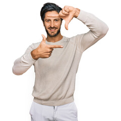 Fototapeta premium Young hispanic man wearing casual clothes smiling making frame with hands and fingers with happy face. creativity and photography concept.
