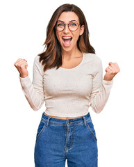 Young brunette woman wearing casual clothes and glasses celebrating surprised and amazed for...