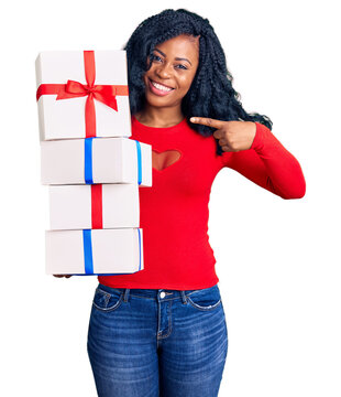 Beautiful african american woman holding presents smiling happy pointing with hand and finger