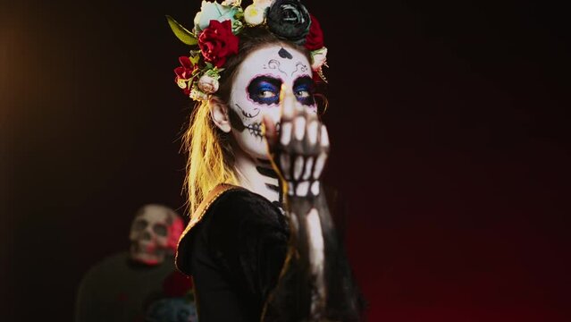 Cavalera catrina luring victims and reaching with hand, tempting and looking flirty on mexican halloween. Lady of death acting horror with skull make up and goddess costume. Handheld shot.