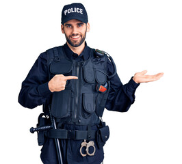 Young handsome man with beard wearing police uniform amazed and smiling to the camera while...