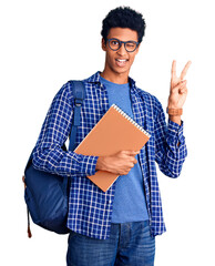 Young african american man wearing student backpack holding book smiling with happy face winking at the camera doing victory sign with fingers. number two.