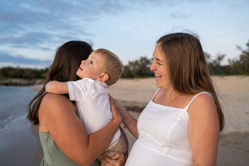 lesbian family on beach with toddler hugging mom