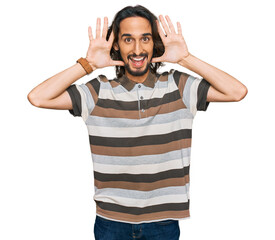 Fototapeta premium Young hispanic man wearing casual clothes smiling cheerful playing peek a boo with hands showing face. surprised and exited