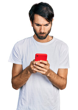 Hispanic man with blue eyes using smartphone typing message skeptic and nervous, frowning upset because of problem. negative person.