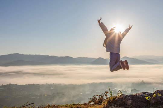 Happy child girl with open arms jumping on the top of foggy mountain morning sunrise