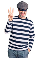 Middle age handsome man wearing burglar mask showing and pointing up with fingers number three while smiling confident and happy.