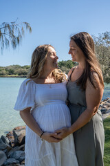 Pregnant lesbian couple embracing in hug at park