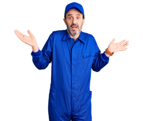 Middle age handsome man wearing mechanic uniform clueless and confused expression with arms and hands raised. doubt concept.