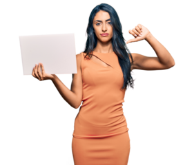 Beautiful hispanic woman holding blank empty banner with angry face, negative sign showing dislike with thumbs down, rejection concept