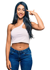 Beautiful hispanic woman wearing casual clothes smiling pointing to head with one finger, great idea or thought, good memory