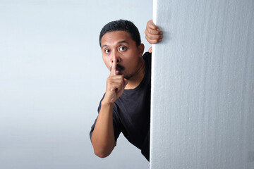 man peeking behind wall with silent gesture