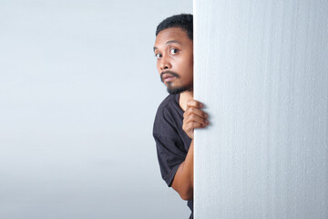 funny curious man peeking behind the wall